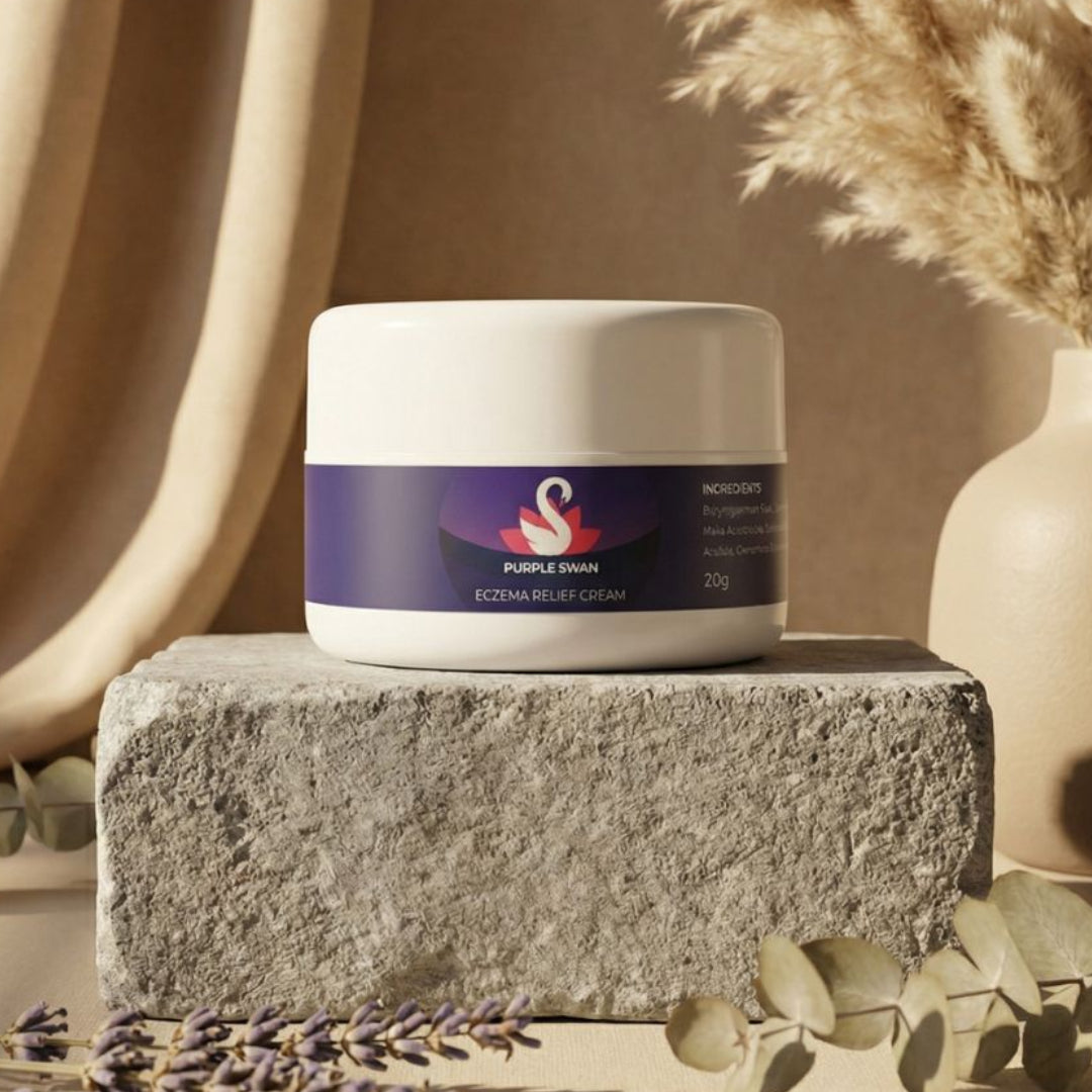 Jar of cream with a purple label on a stone surface, surrounded by lavender and a vase with dried plants.