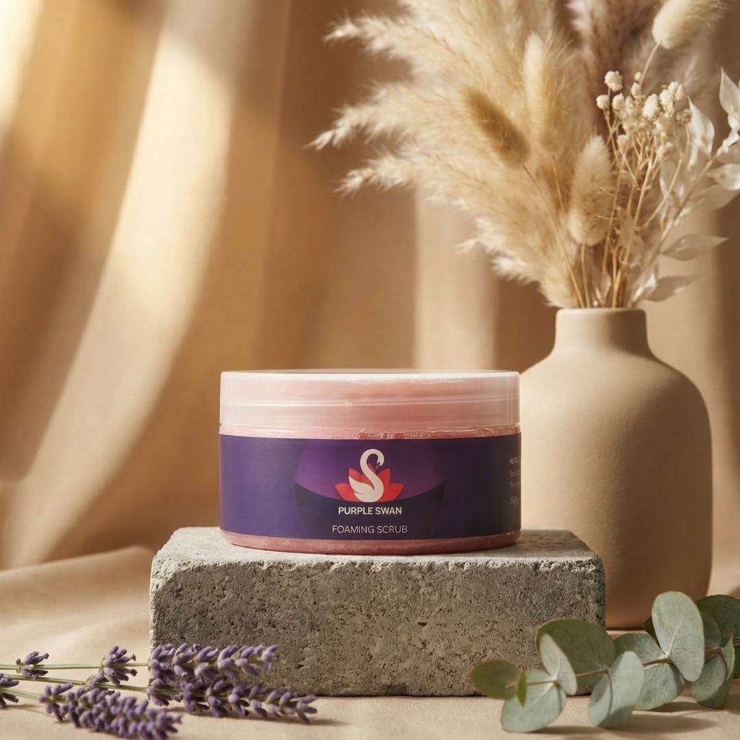 Jar of 'Purple Swan' foaming scrub on a stone block with a vase of dried flowers and lavender in the background.