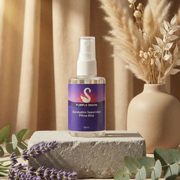 Purple Swan Eucalyptus Spearmint Pillow Mist displayed on a stone pedestal with dried pampas grass and lavender decor.
