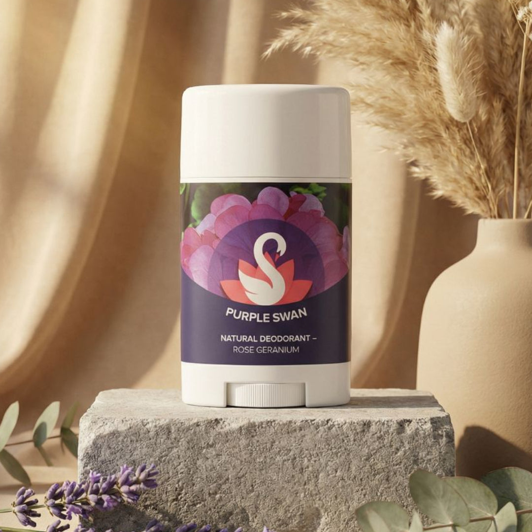 Purple Swan natural deodorant on a stone block with lavender and eucalyptus leaves, against a beige curtain background.